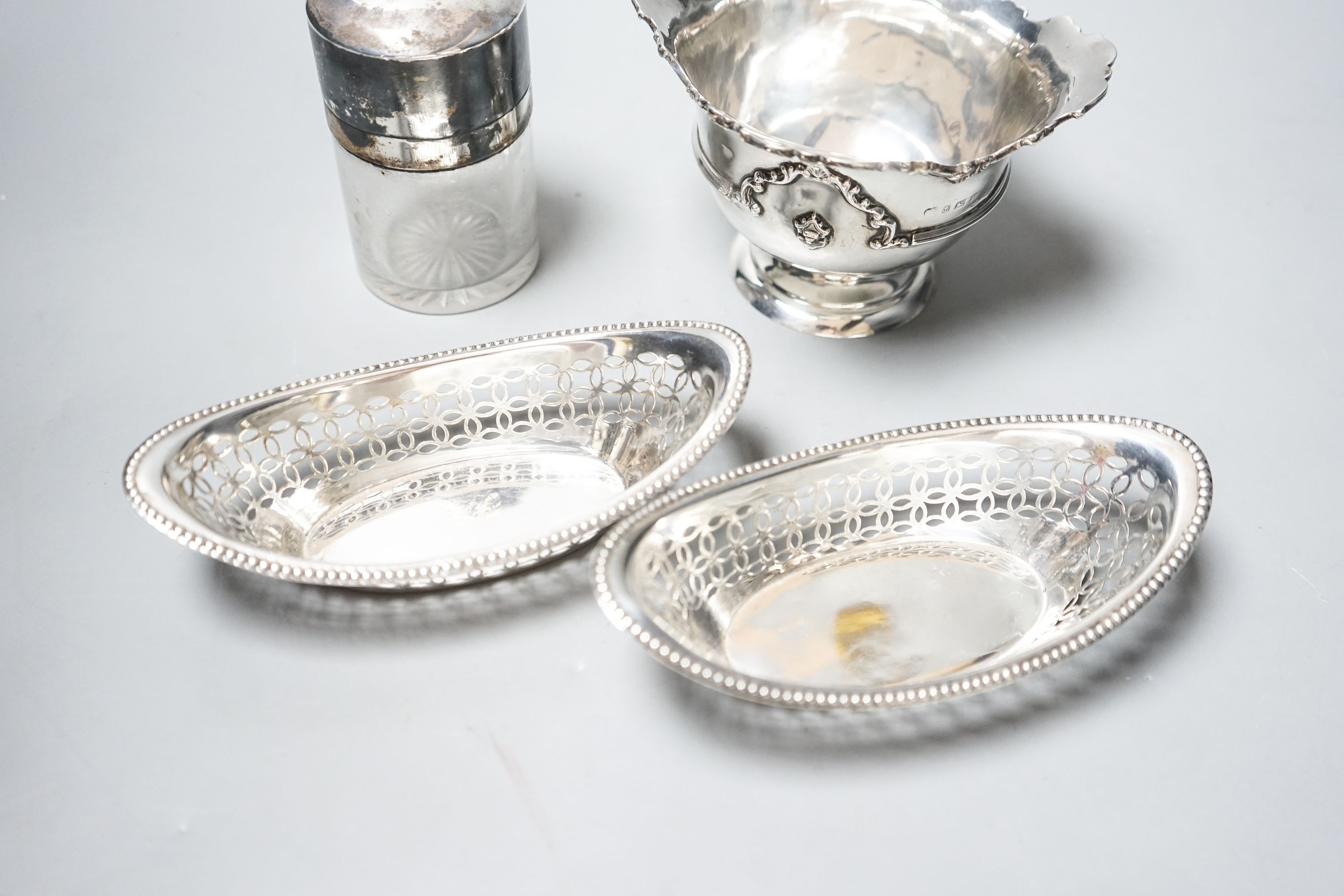 A pair of Edwardian silver oval bon bon dishes, a George V silver sugar bowl and a silver mounted glass smelling salts bottle.